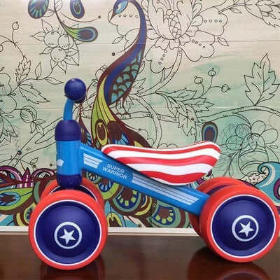 Plastic no-pedal kids balance bike with three wheels in US Team theme, featuring a blue frame and striped seat against a colorful background.