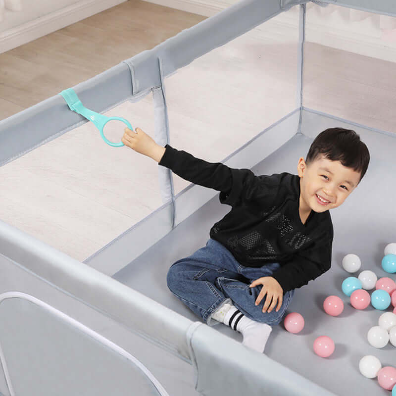 Child playing in a gray indoor play fence with colorful balls, ensuring safety and fun for ages 0 to 3 years old.